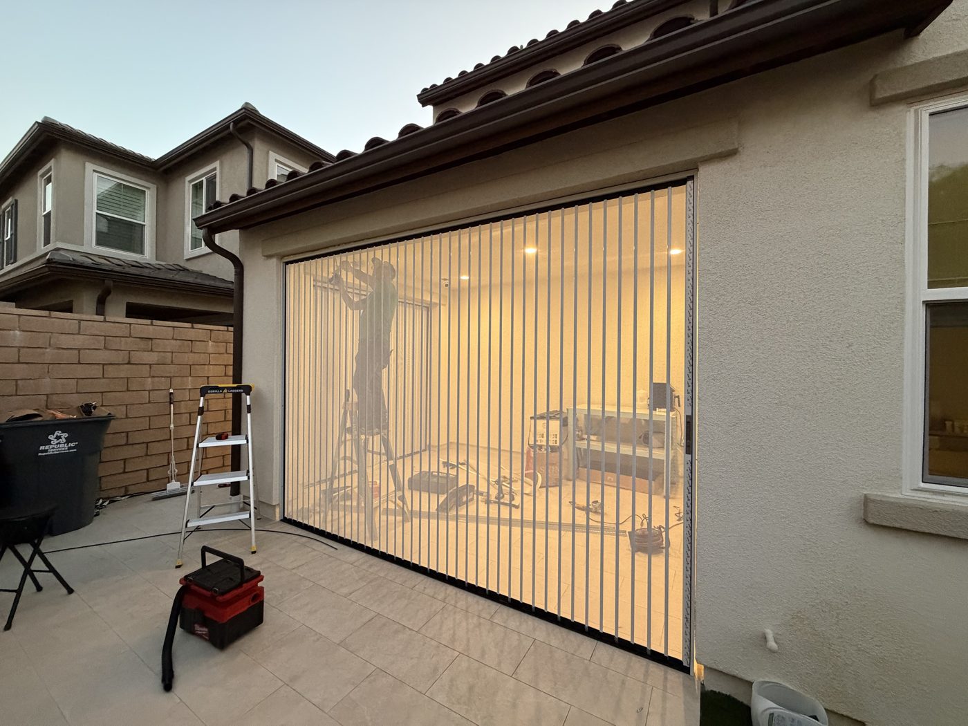 Wide white folding screen across a garage opening, seen from the driveway