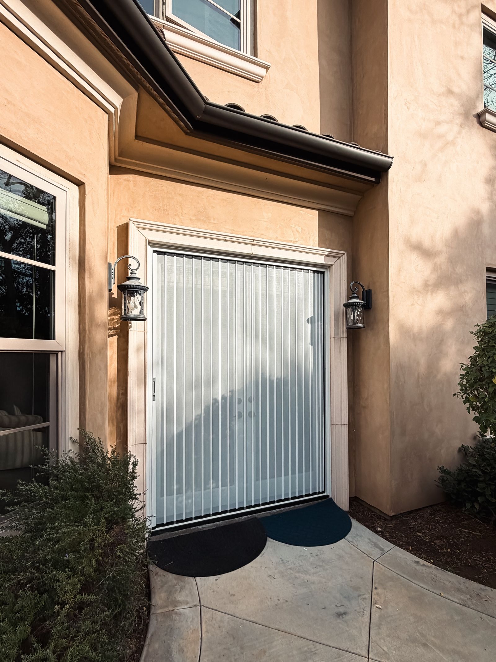 A white SolSeen folding screen closed across stucco French doors in afternoon light