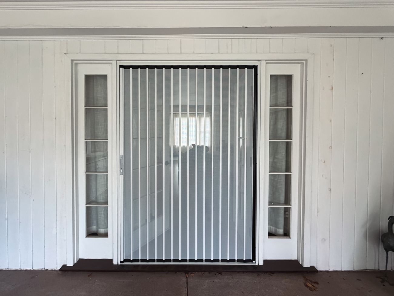 White folding screen across a wide door with glass sidelights in a white paneled porch